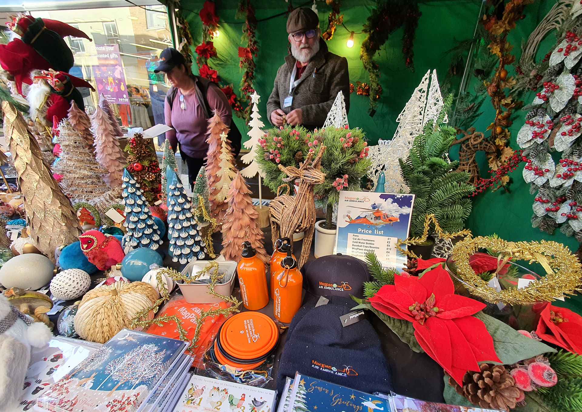 A market stall packed with colourful Christmas decorations, from small Christmas trees to warm hats, Christmas wreaths and hot water flasks.