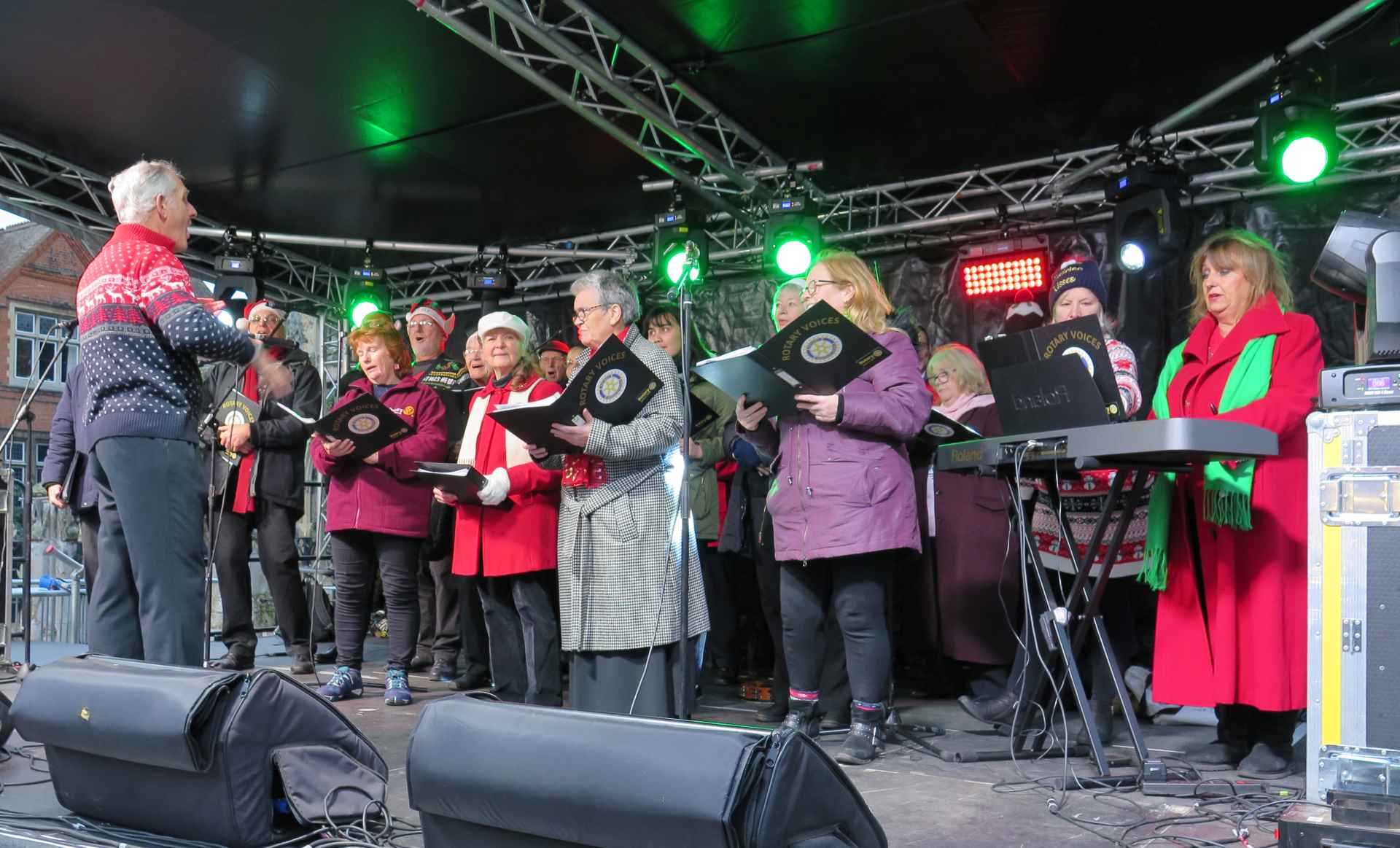 A choir singing on stage holding their hymn books with a conductor leading them.
